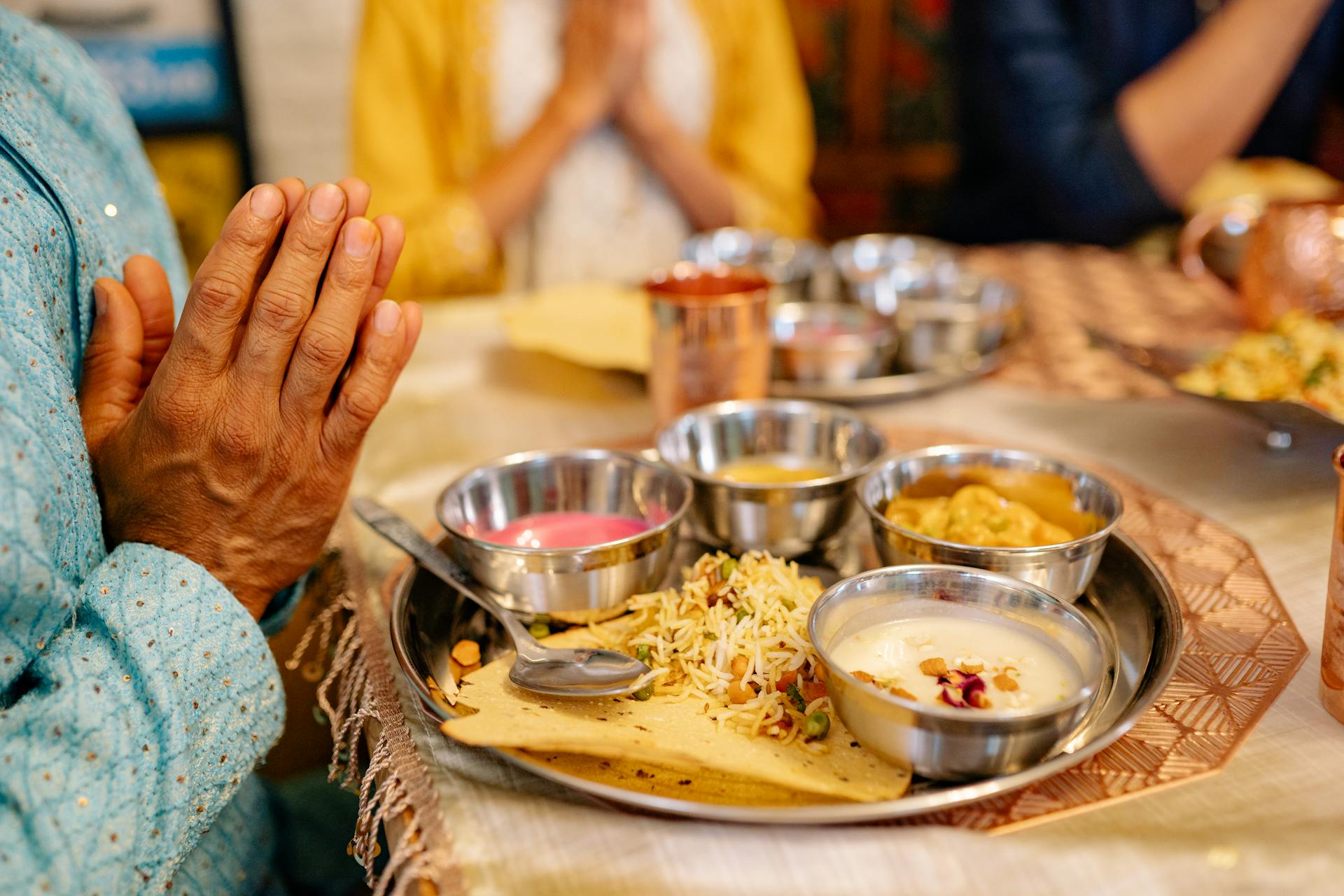 Hands in prayer near a simple thali. A moment of intention before eating.